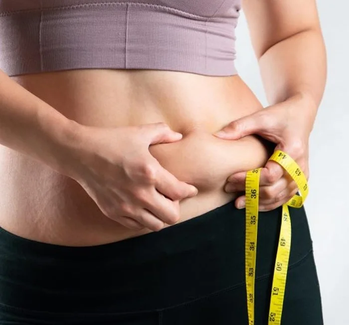 Person measuring their waistline with a tape measure while working toward a healthy weight