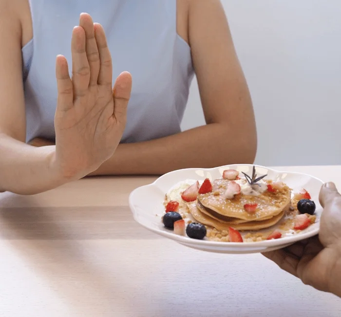 Woman practising everyday appetite control by declining a plate of pancakes